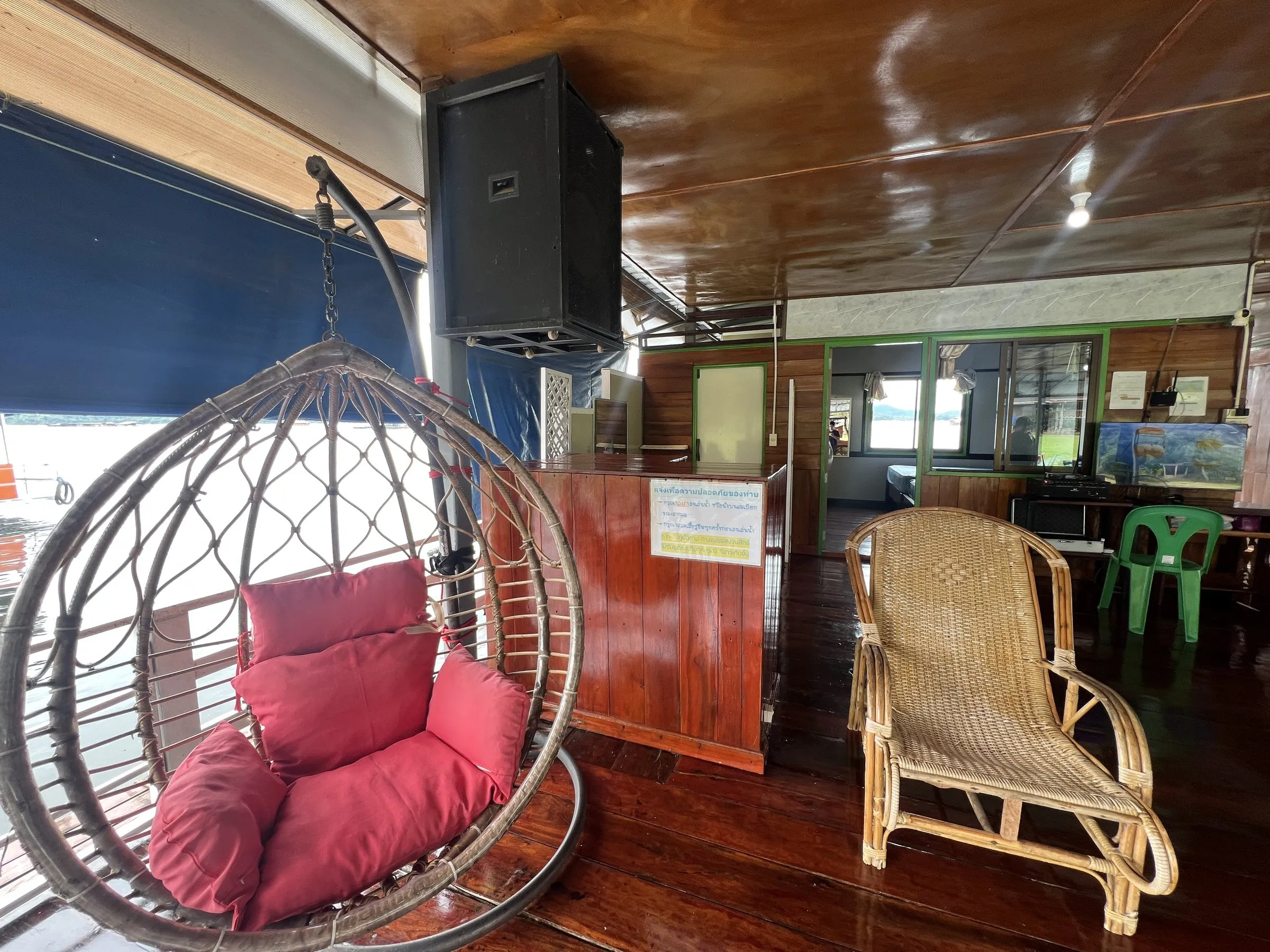 A hanging egg chair with a red cushion on the varnished deck of the raft house.