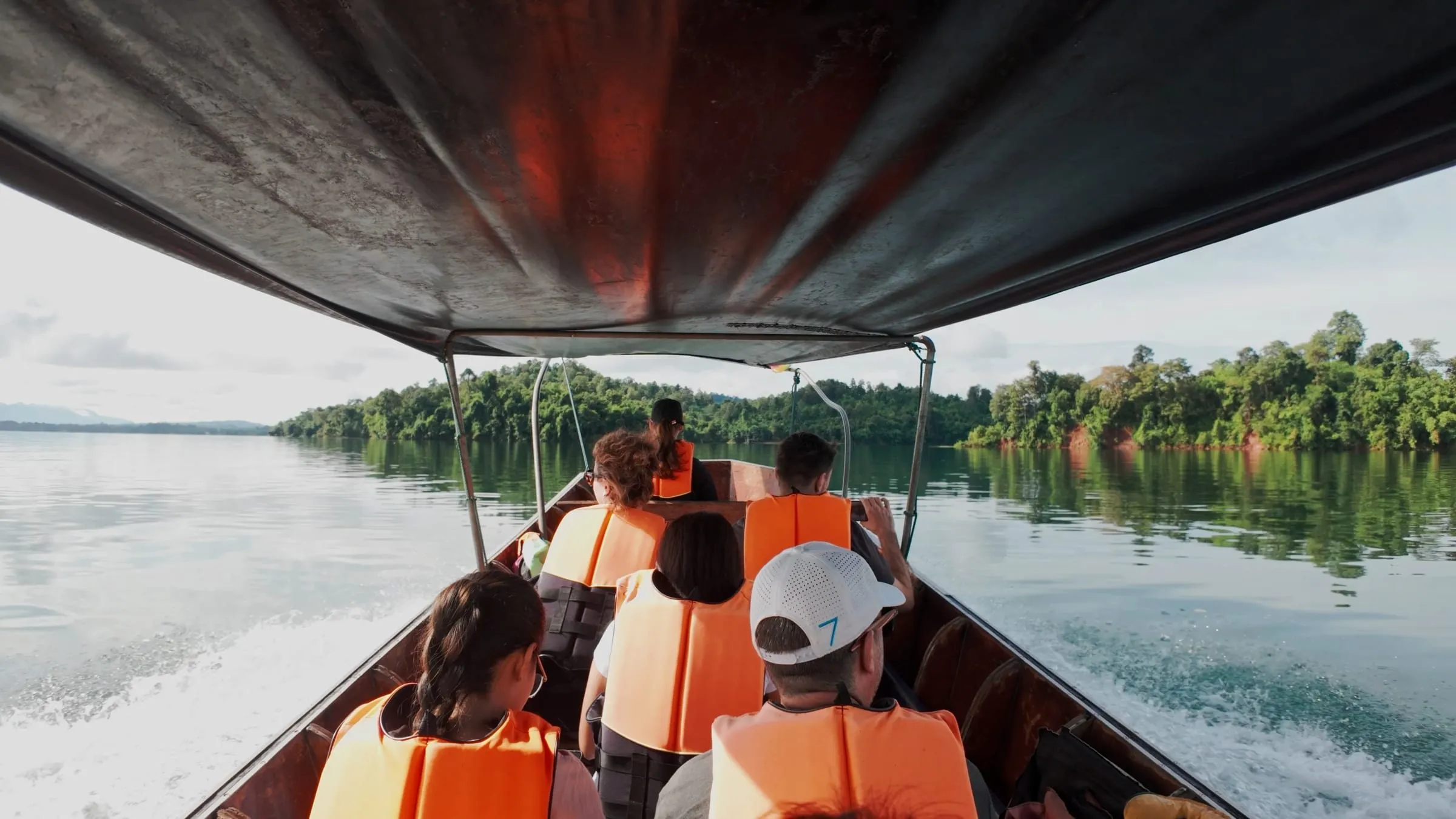 Passengers in life jackets under the canopy of a longtail boat crossing the lake.