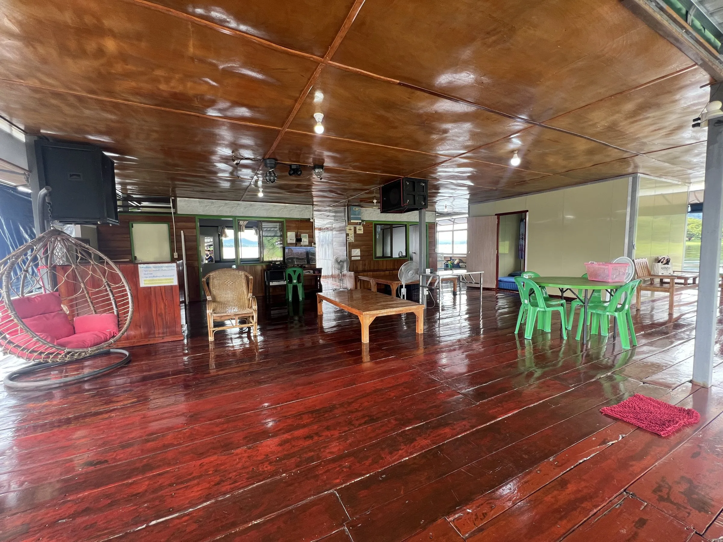 The wide varnished deck of the raft house with chairs, a low table and the lake beyond.