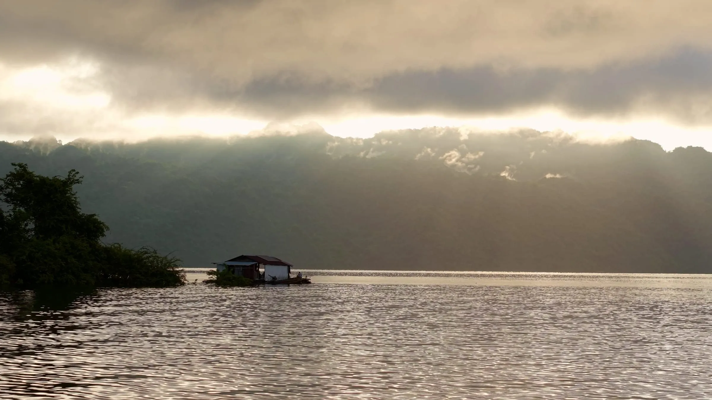 Late sun breaking under heavy cloud over the wide open water of Khao Laem Lake.