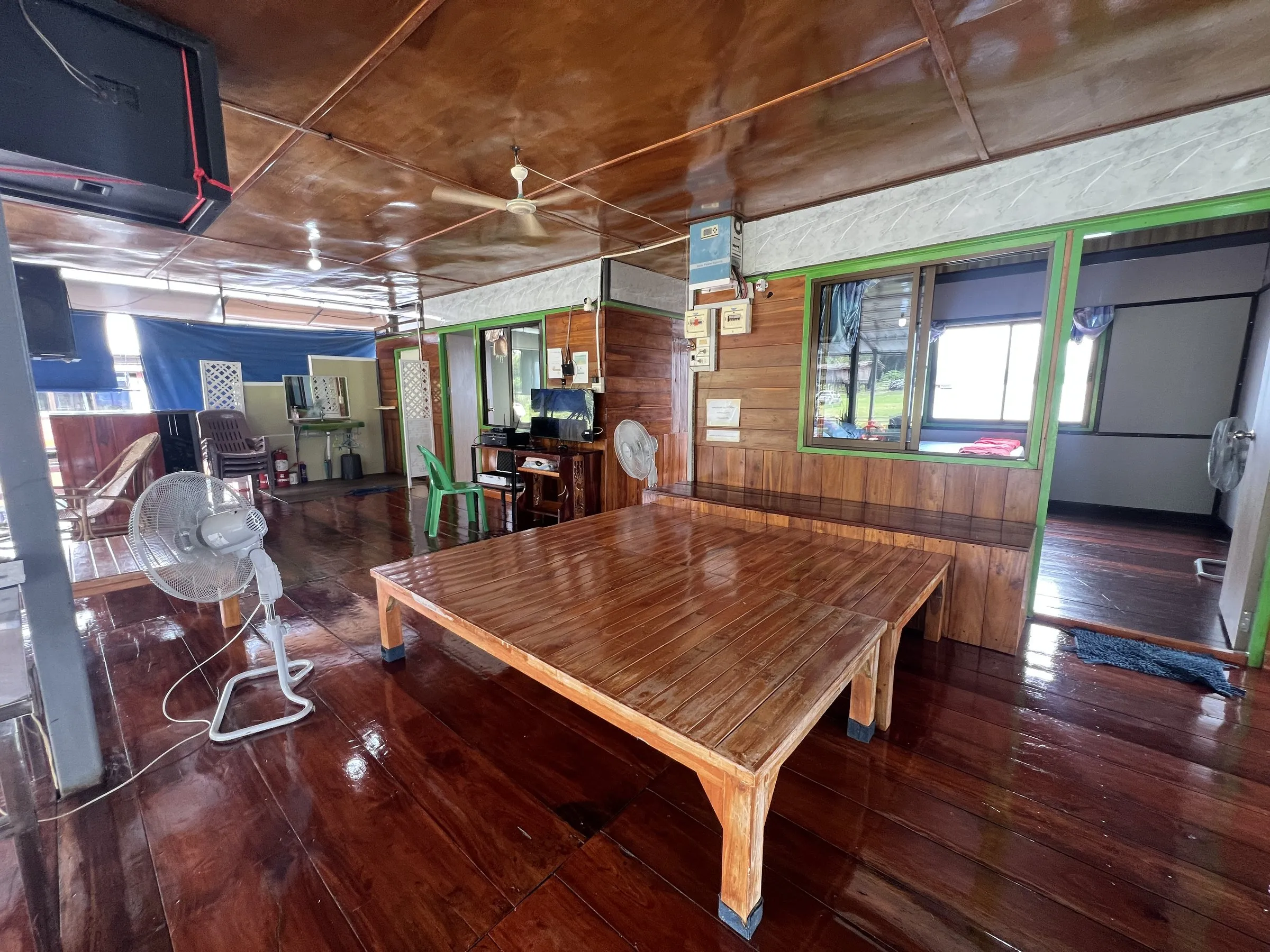 A long low wooden table and a fan on the varnished deck of the raft house.